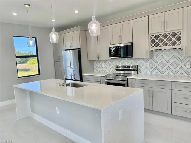 Kitchen featuring gray cabinets, a kitchen island with sink, a sink, stainless steel appliances, and backsplash