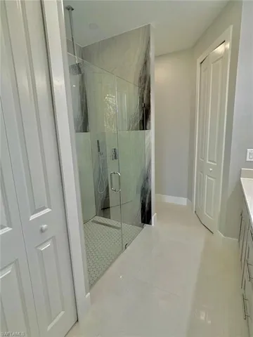 Full bath featuring tile patterned floors, vanity, baseboards, and a marble finish shower