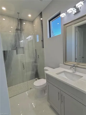 Bathroom with toilet, a marble finish shower, vanity, and recessed lighting