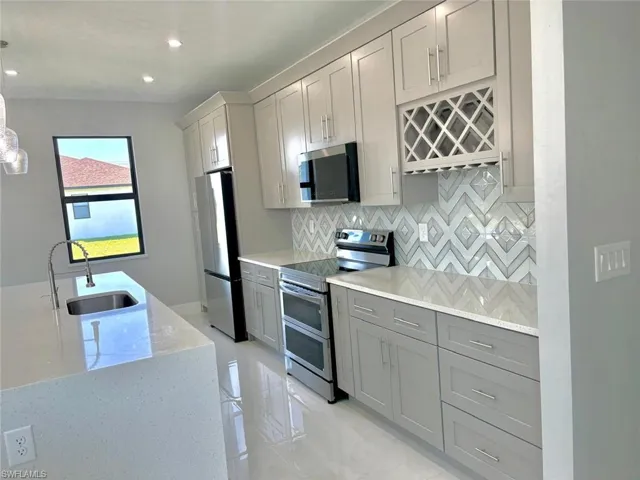 Kitchen with a sink, appliances with stainless steel finishes, gray cabinetry, backsplash, and light stone counters