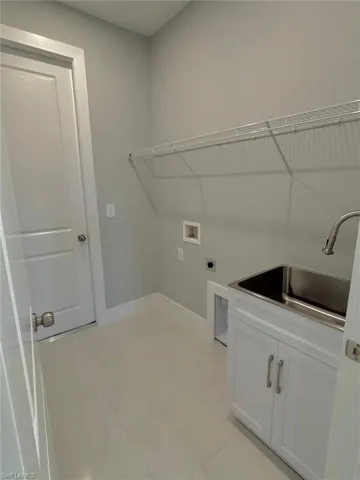 Washroom with hookup for an electric dryer, light tile patterned floors, hookup for a washing machine, cabinet space, and a sink