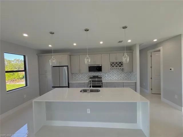 Kitchen with light countertops, appliances with stainless steel finishes, an island with sink, gray cabinetry, and backsplash