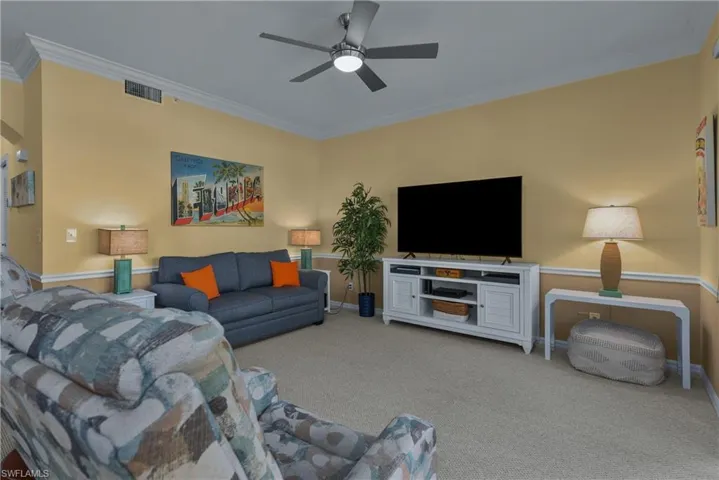 Carpeted living room featuring ceiling fan and ornamental molding