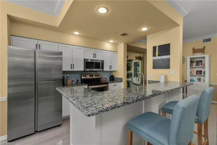Kitchen with stone countertops, white cabinetry, a kitchen bar, kitchen peninsula, and stainless steel appliances
