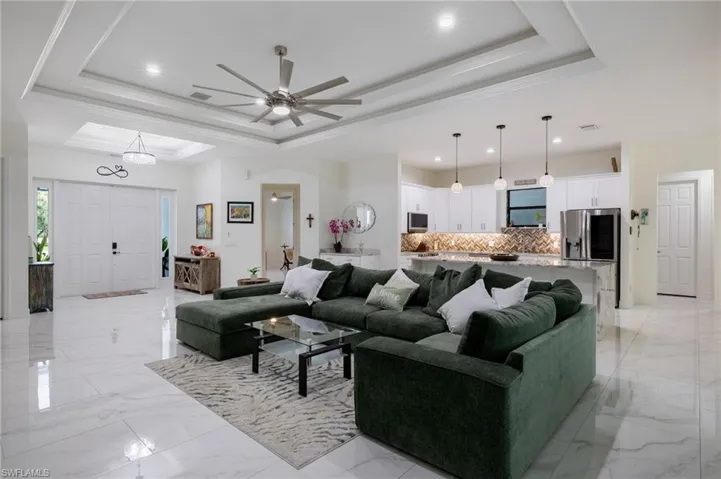 Living room with a tray ceiling, ceiling fan, light marble finish flooring, a glass covered fireplace, and ornamental molding