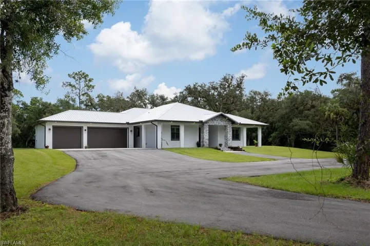 View of front of property with covered porch, a front lawn, an attached garage, driveway, and a metal roof