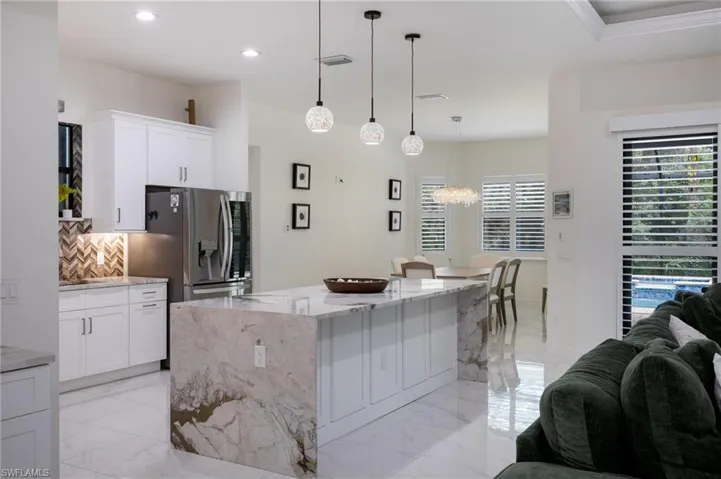 Living room featuring a tray ceiling, ornamental molding, light marble finish floors, ceiling fan, and recessed lighting