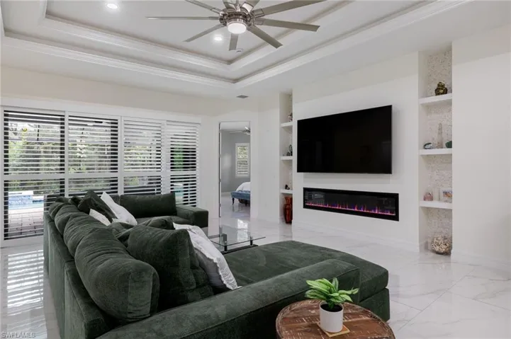 Living area featuring a tray ceiling, light marble finish floors, ornamental molding, recessed lighting, and a ceiling fan
