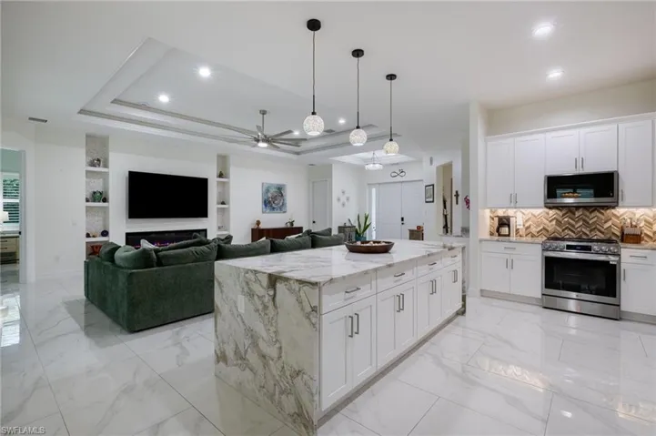 Kitchen with light stone counters, stainless steel appliances, light marble finish flooring, decorative backsplash, and white cabinets