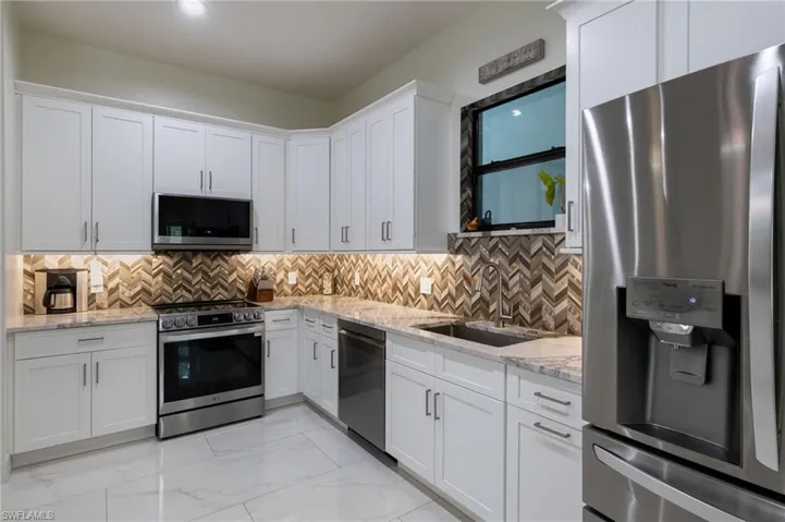 Kitchen with white cabinets, appliances with stainless steel finishes, hanging light fixtures, a center island, and light stone countertops