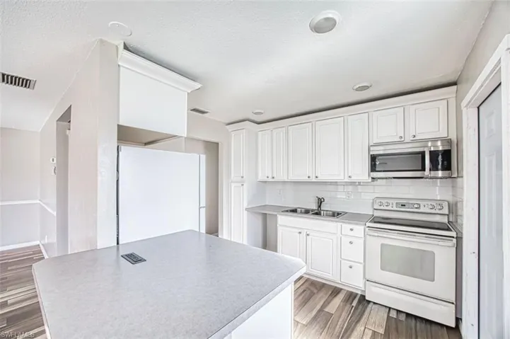Kitchen featuring white appliances, white cabinets, light wood finished floors, backsplash, and light countertops