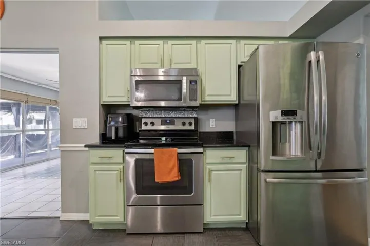 Kitchen with dark stone countertops, green cabinetry, dark tile patterned flooring, and stainless steel appliances