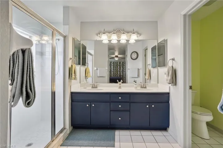 Bathroom with a shower with door, tile patterned flooring, toilet, ceiling fan, and double sink vanity