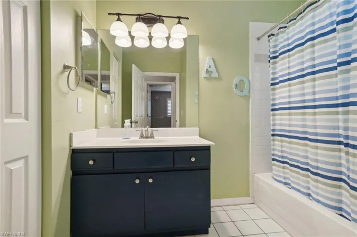 Bathroom with vanity, shower / bathtub combination with curtain, and tile patterned flooring