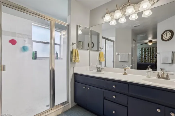 Bathroom with dual vanity, a shower with door, and ceiling fan