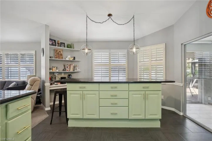 Kitchen with green cabinets, dark tile patterned flooring, decorative light fixtures, and a kitchen bar