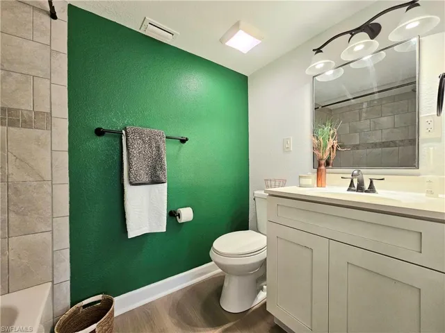 Bathroom with vanity, dark wood-type flooring, a textured wall, and shower / bathtub combination
