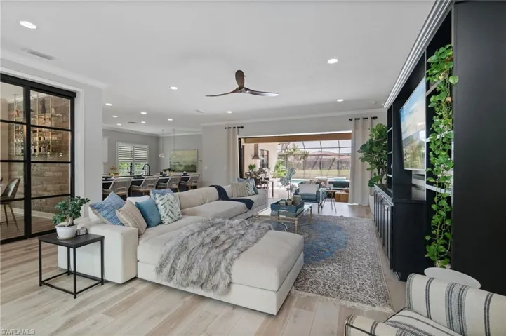 Expansive open Great Room Living area with ornamental crown molding, light wood-style floors, decorative ceiling fan, and abundant recessed lighting.  A stunning pool and lake view and abundant entry and foyer lighting feel bright and modern.