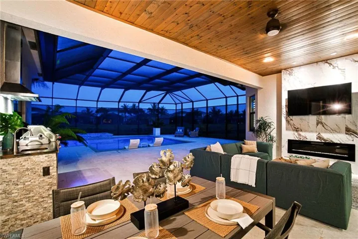 Pocketing panels of impact glass open to a custom tile stone look fireplace seating area with dining and summer kitchen for an entertainer’s DREAM!