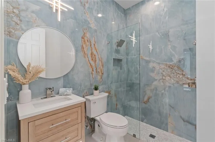 LA style full wall tiles stone look downstairs pool Bathroom with designer wood floating vanity, and a stunning walk in shower enclosure with frameless glass.