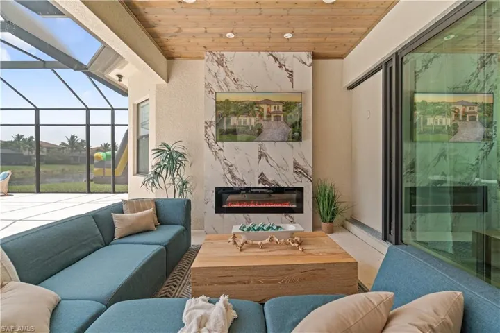 Outdoor Dining space with planked ashwood wooden ceiling, paneled glass impact sliding entry doors bringing the outside in, airy ceiling fan, and a cozy stone look custom outdoor gas fireplace for cool winter nights!