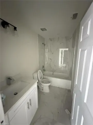 Full bathroom featuring a combined bath / shower with marble appearance, vanity, and marble look tile flooring