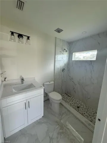 Bathroom with vanity, light marble finish floors, and a marble finish shower