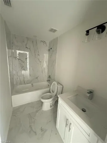Bathroom featuring vanity, a combined bath / shower with marble appearance, and light marble finish floors