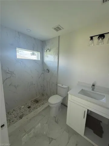 Bathroom featuring a marble finish shower, vanity, and light marble finish flooring