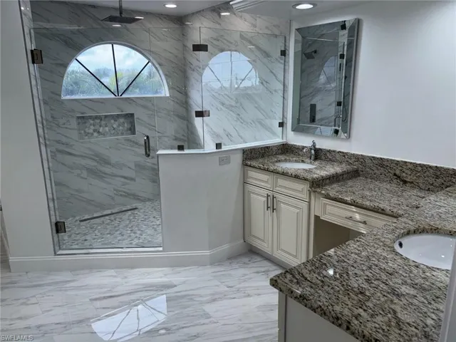 Main Bathroom featuring two vanities, a marble finish shower, and light Polished Porcelain finish flooring