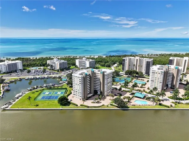 Waterfront high-rise community featuring exterior swimming pool, manicured grounds, and paved parking area, situated on a coastal peninsula