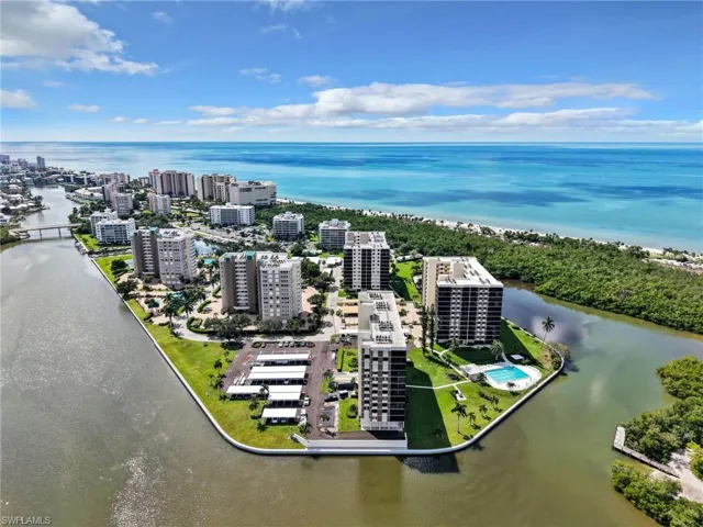 Aerial perspective of a multi-building residential community featuring direct water access, a private marina, paved parking areas, and on-site recreational courts