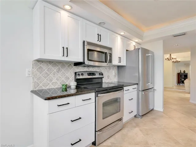 Kitchen featuring white cabinetry with matte black hardware, dark stone countertops, stainless steel appliances, recessed ceiling lighting with crown molding, and tile flooring