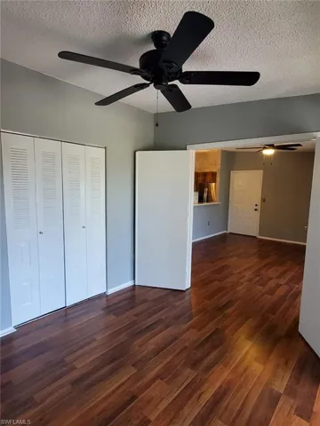 Unfurnished bedroom featuring dark wood-style floors, a textured ceiling, stainless steel fridge, a ceiling fan, and a closet