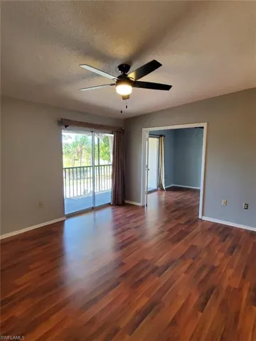 Empty room featuring a textured ceiling, dark wood-type flooring, and a ceiling fan