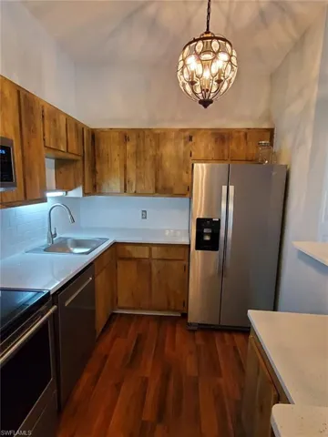 Kitchen with stainless steel appliances, dark wood-style floors, wood finish cabinets, and suspended lighting