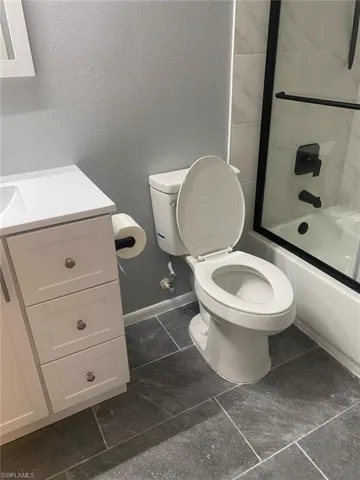 Bathroom featuring vanity, combined bath / shower with glass door, and a textured wall