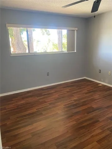 Empty room with dark wood-type flooring, a textured ceiling, and a ceiling fan