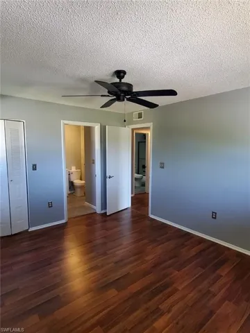 Unfurnished bedroom featuring a textured ceiling, dark wood-style flooring, ceiling fan, ensuite bath, and a closet