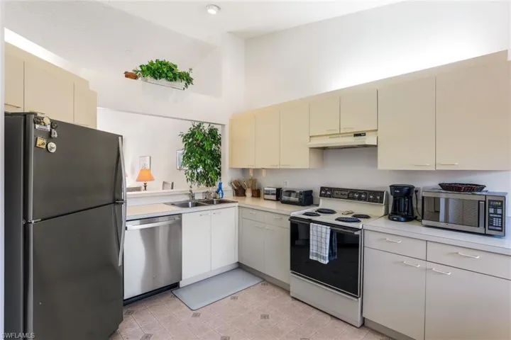Kitchen with cream cabinets, stainless steel appliances, light countertops, under cabinet range hood, and lofted ceiling