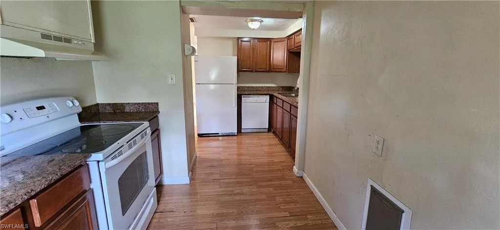 Kitchen with light hardwood / wood-style flooring, dark stone countertops, white appliances, and ventilation hood