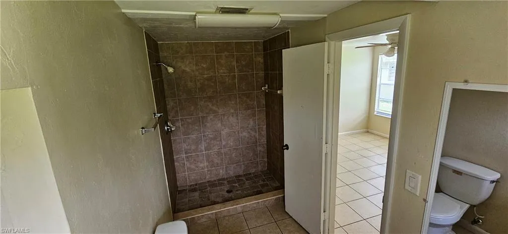 Bathroom featuring tile patterned flooring, tiled shower, ceiling fan, and toilet