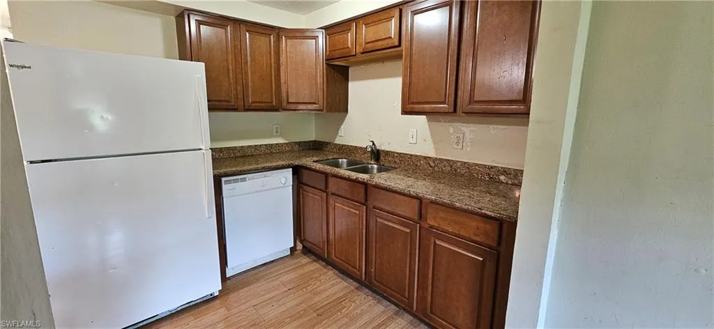 Kitchen with dark stone countertops, light wood-type flooring, sink, and white appliances