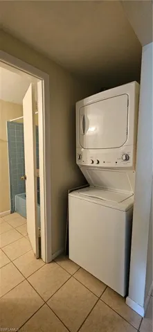 Clothes washing area with light tile patterned floors and stacked washer and clothes dryer