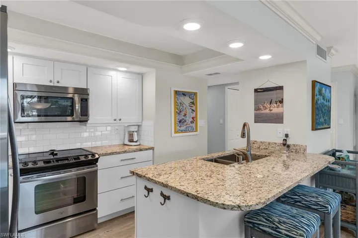 Kitchen featuring a sink, light stone counters, tasteful backsplash, appliances with stainless steel finishes, and a peninsula
