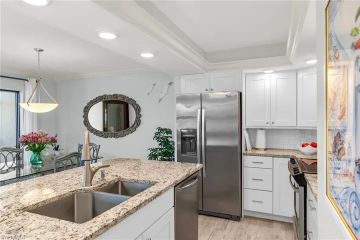 Kitchen featuring light stone countertops, a sink, appliances with stainless steel finishes, white cabinetry, and crown molding
