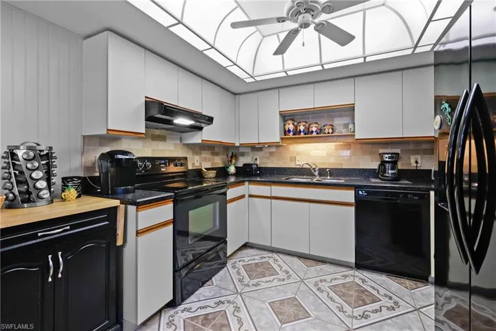 Kitchen featuring under cabinet range hood, black appliances, a ceiling fan, a sink, and decorative backsplash