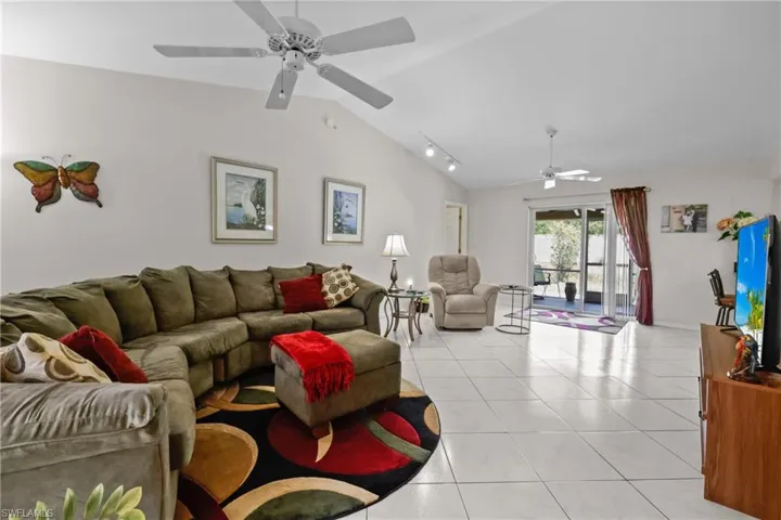 Living area featuring lofted ceiling, ceiling fan, light tile patterned flooring, and rail lighting
