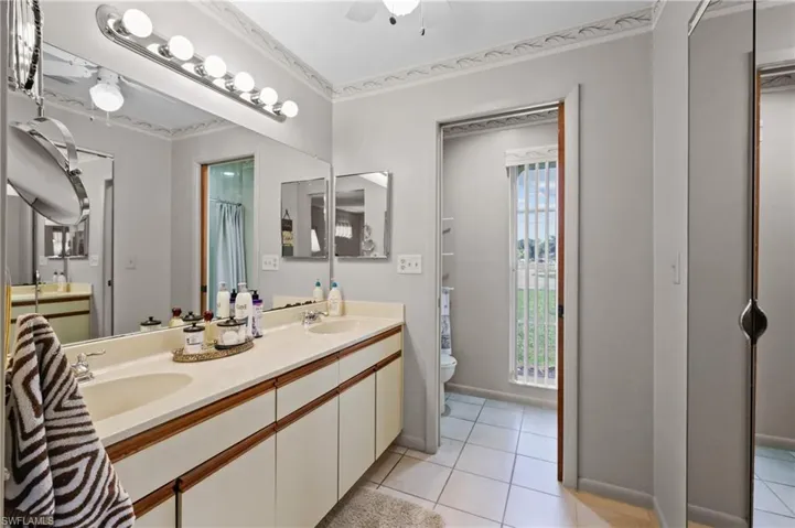Bathroom with toilet, tile patterned flooring, double vanity, baseboards, and crown molding