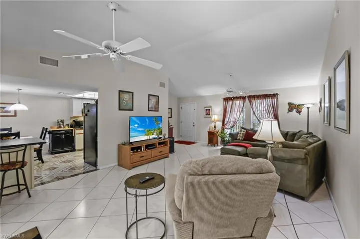 Living area featuring light tile patterned flooring, a ceiling fan, vaulted ceiling, and baseboards